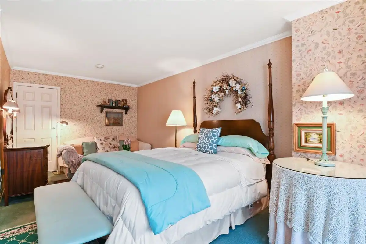 A queen bed and bedside table against peach floral wallpaper, with a couch positioned on the adjacent wall.