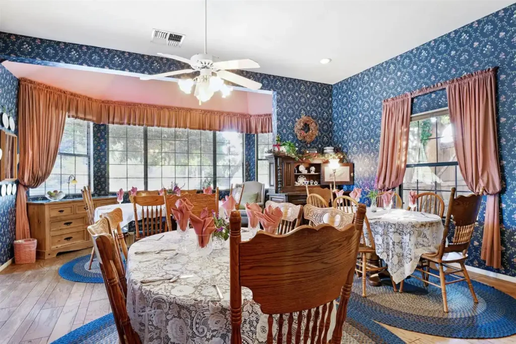 A wooden table and chairs with a lace tablecloth in a blue floral dining room.