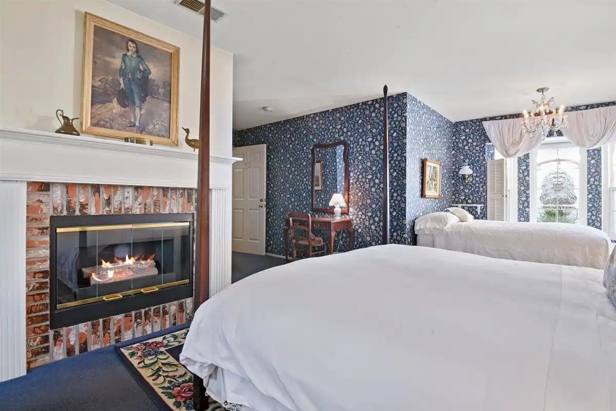 An oil painting hangs above a brick fireplace in a room positioned near a king bed and a full bed.