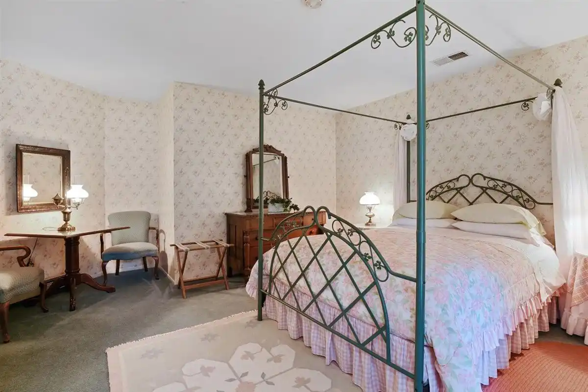 Queen canopy poster bed positioned next to a wooden vanity against a pastel floral wallpaper.