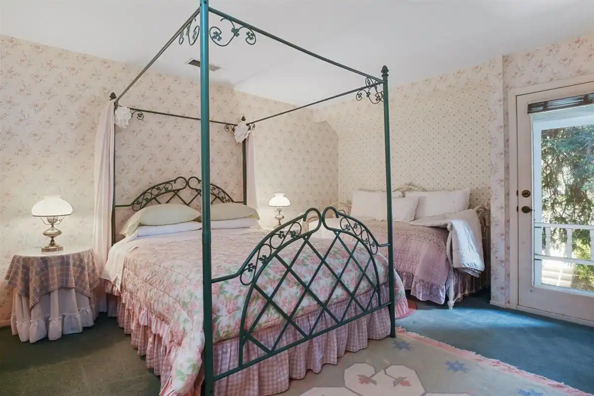 Queen canopy poster bed against a pastel floral wallpaper.